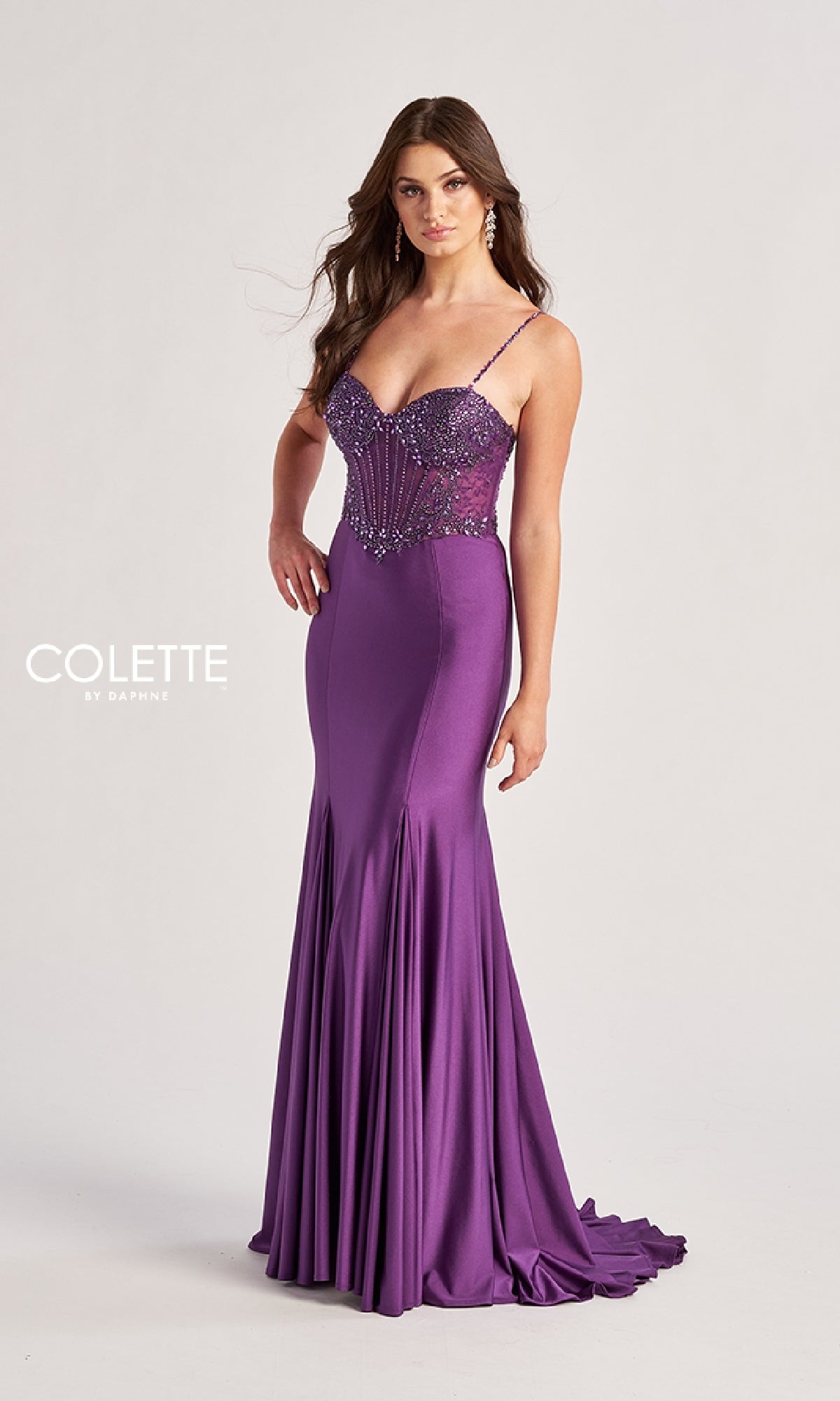 A woman models the Long Prom Dress: Colette CL8515, a fitted, floor-length purple mermaid gown with thin straps and beaded embellishments, posing against a plain white background.